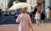 Alte Frau mit Sonnenschirm geht auf einer Straße spazieren.