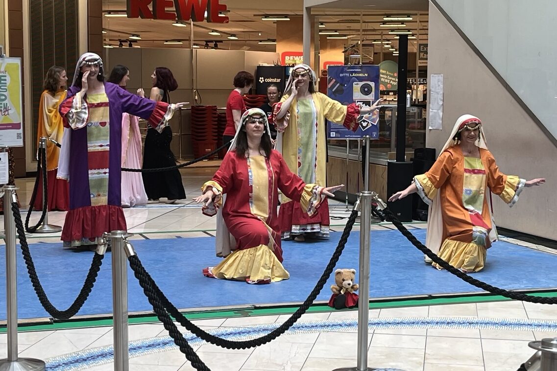 Vier Frauen in langen, bunten Gewändern auf einer Bühne, zwei knien vorn, zwei stehen hinten.