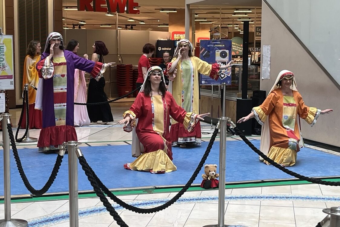 Vier Frauen in langen, bunten Gewändern auf einer Bühne, zwei knien vorn, zwei stehen hinten.