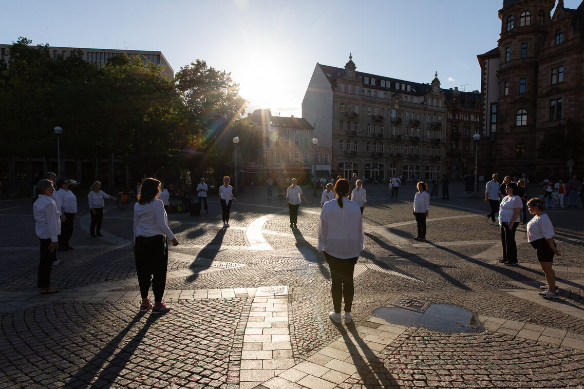 Frauen stehen im Kreis auf dem Dernschen Gelände. Die Sonne verleiht der Szenerie eine besondere Atmosphäre.
