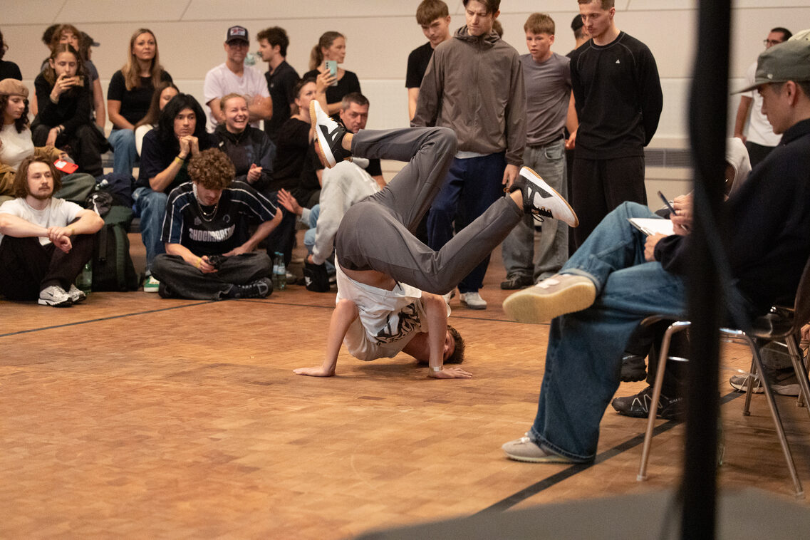 Breakdance: Eine Person stützt sich auf die Unterarme und den Kopf. Die Beine sind angewinkelt in der Luft.