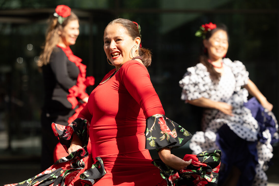Eine Frau im roten Flamencokostüm und roten Blumen im Haar dreht sich in die Kamera und schwingt ihren Rock.