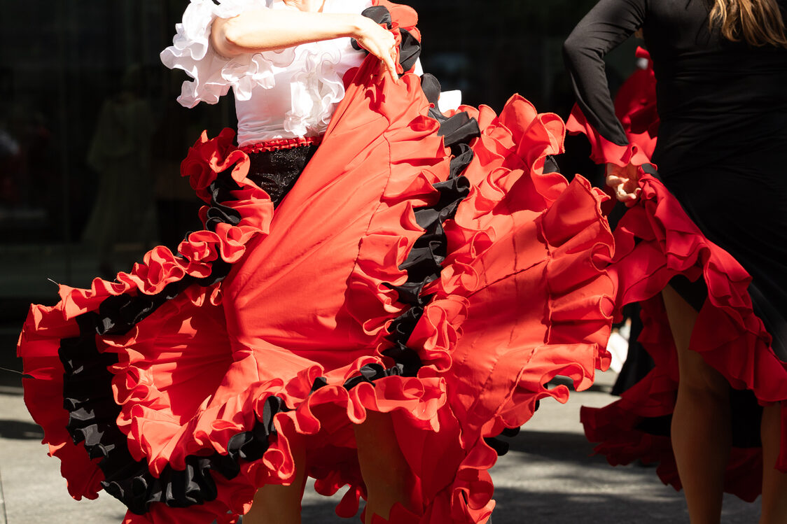 Eine Frau in weißer Bluse und roten Rock (beides mit Rüschen) schwingt ihren Rock.