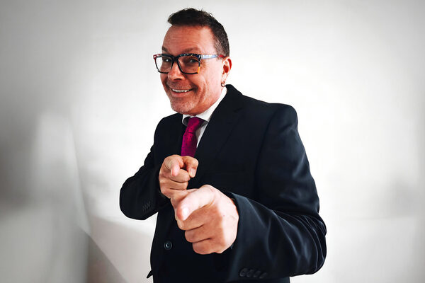 Mann mit großer Brille und gestreckten Zeigefingern schaut in Kamera.