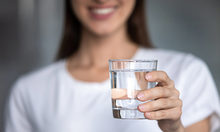 Frau im weißem Shirt - und abgeschnittenem Gesicht - hält Wasserglas