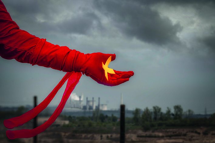 Arm mit rotem Handschuh, Vogel in der Hand, im Hintergrund Fabrik